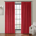 Vibrant red pleated velvet curtains on a black rod framing a multi-pane window in a modern living space featuring a minimalist tree artwork and a beige armchair with a textured cream throw