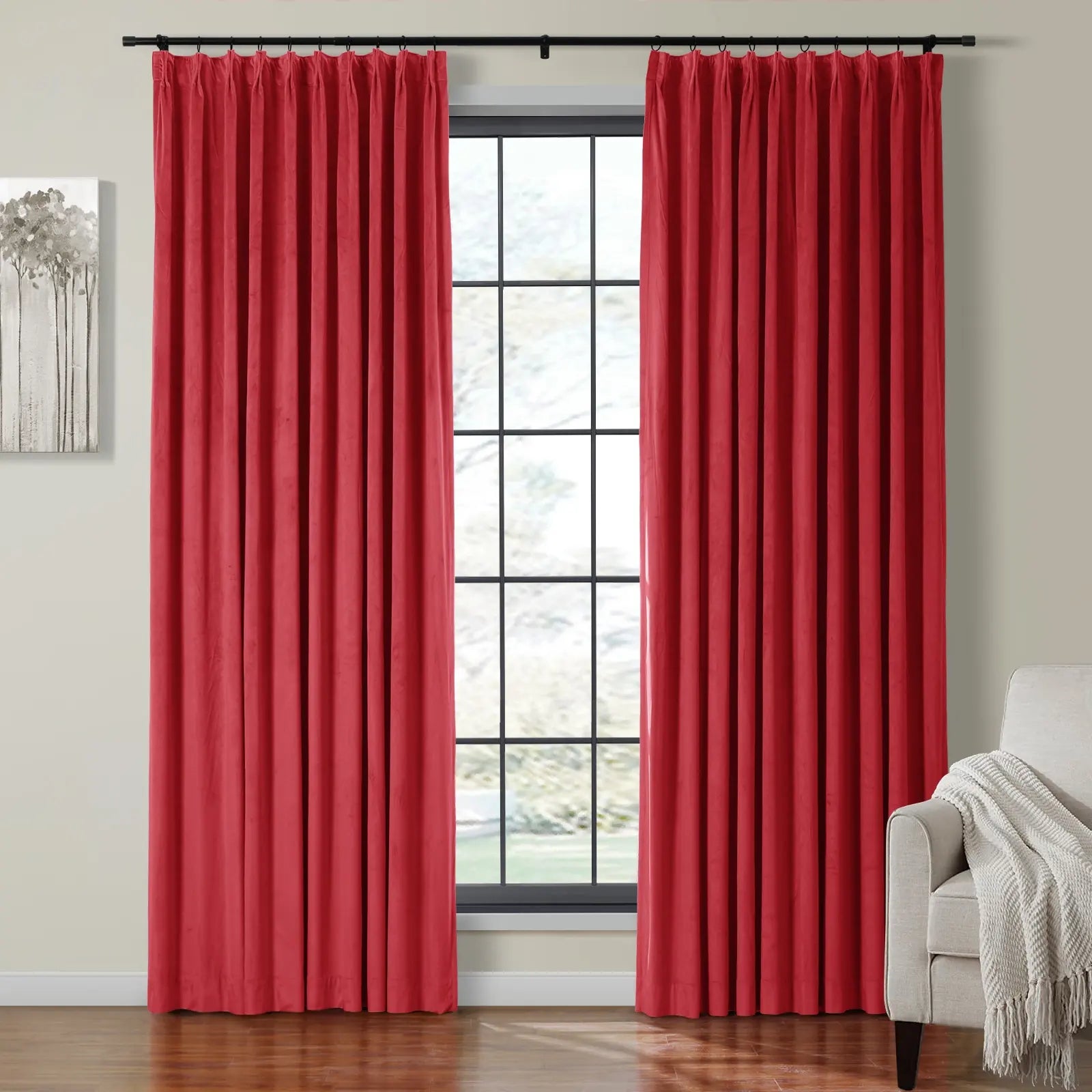 Vibrant red pleated velvet curtains on a black rod framing a multi-pane window in a modern living space featuring a minimalist tree artwork and a beige armchair with a textured cream throw