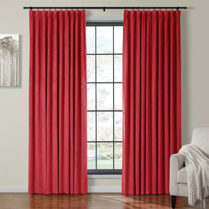 Vibrant red pleated velvet curtains on a black rod framing a multi-pane window in a modern living space featuring a minimalist tree artwork and a beige armchair with a textured cream throw
