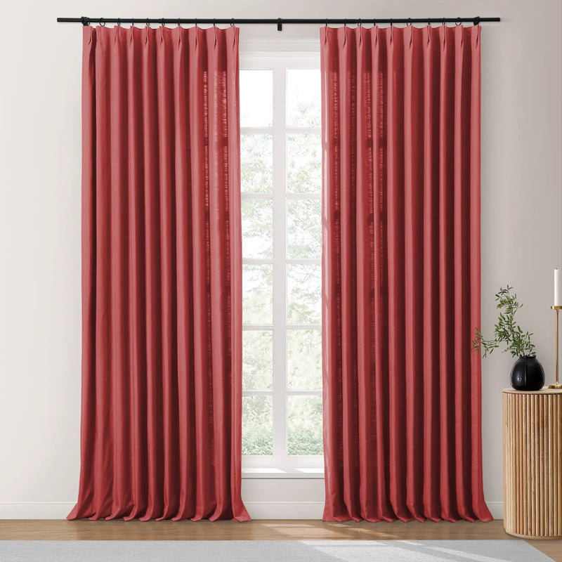 Faux silk rich rust-red pleated curtains on a black rod frame a sunlit window revealing green trees, accented by a fluted wood table with a black vase and gold candlestick