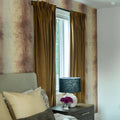 Elegant bedroom interior with plush brown velvet curtains, abstract earthy-toned wallpaper, a dark grey textured lamp shade, and a small vase of vibrant purple flowers on a dark wood nightstand