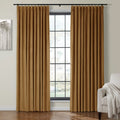 A pair of warm caramel pleated curtains framing a large grid-style window in a cozy room with abstract tree art and a light gray armchair draped with a white throw