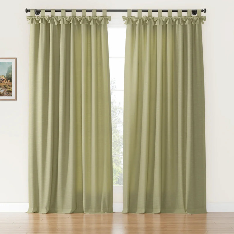 Sage green linen-look tab-top curtains featuring decorative ruffled tops hung on a black rod in a bright room with a hardwood floor and a small framed landscape painting on the wall