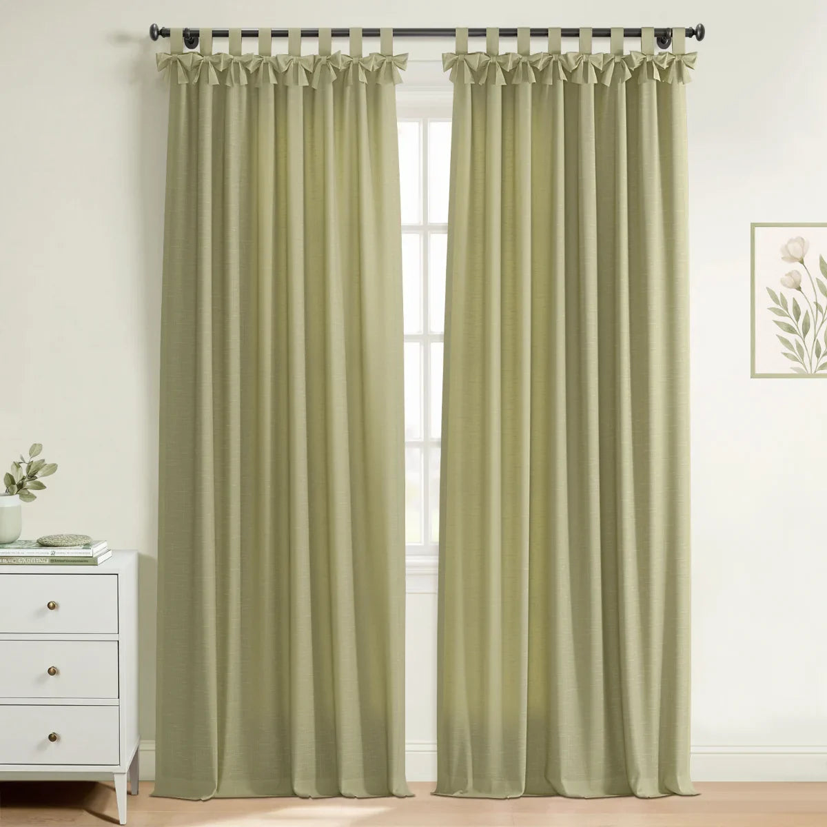 Photograph of light olive green tab top curtains with ruffled detailing in a bright room featuring a white dresser and botanical print wall art