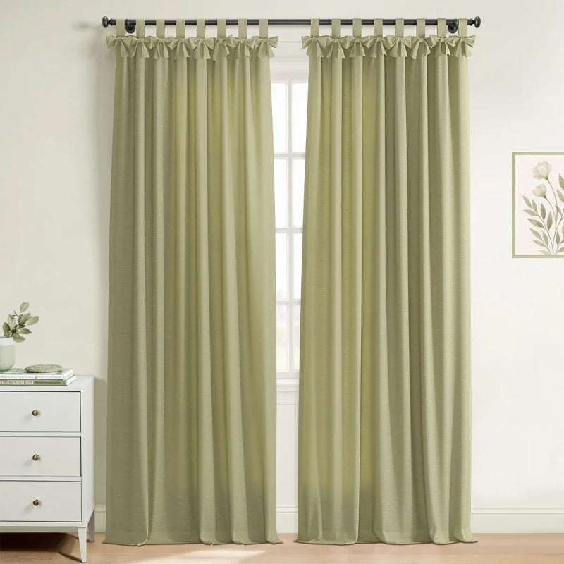 Photograph of light olive green tab top curtains with ruffled detailing in a bright room featuring a white dresser and botanical print wall art