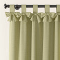 Light green linen-textured curtains with decorative bow-tied tab tops hanging on a dark metal curtain rod featuring a round finial