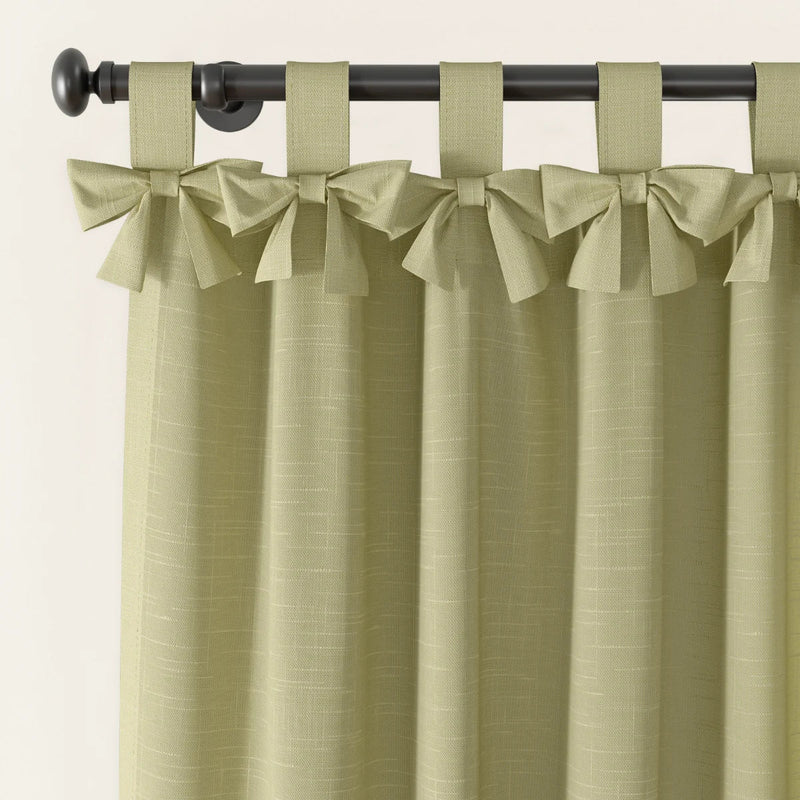 Light green linen-textured curtains with decorative bow-tied tab tops hanging on a dark metal curtain rod featuring a round finial