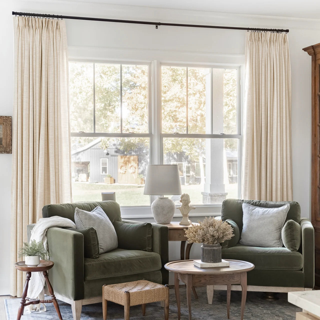 Sand Beige Liz Linen Pleated Curtains framing a green sofa beneath a wide sunlit window