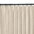 Photograph of a light beige curtain with a subtle linen texture hanging in neat pleats from a black curtain rod with dark rings