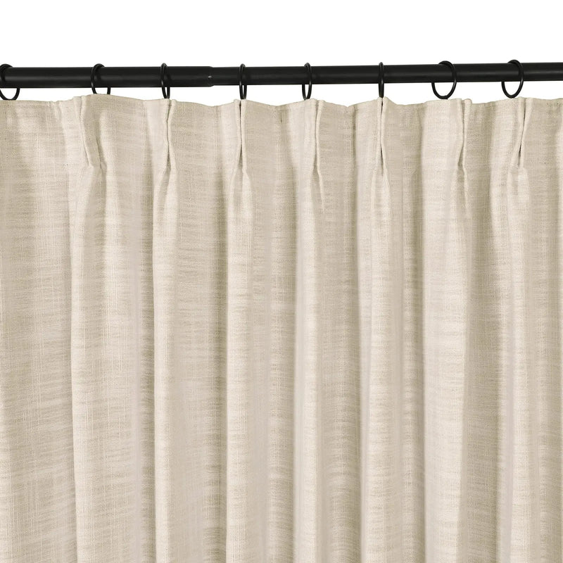 Photograph of a light beige curtain with a subtle linen texture hanging in neat pleats from a black curtain rod with dark rings