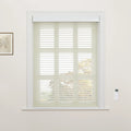 Interior view of a room featuring a large window with light cream zebra Blinds and white ornate trim, a white remote control mounted on the wall to the right, and a framed botanical art print on the left