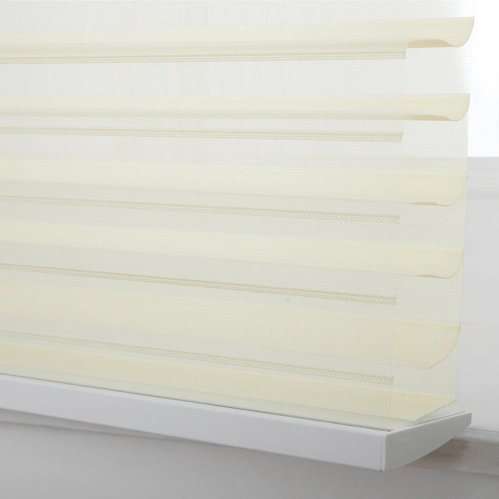 Close-up of cream day-night zebra Blinds in a window featuring alternating translucent and opaque horizontal stripes and a white bottom rail with a subtle 'Light' brand logo