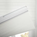 White layered window Blinds with a textured horizontal stripe pattern featuring a visible white headrail with a silver accent partially lowered to reveal outdoor foliage