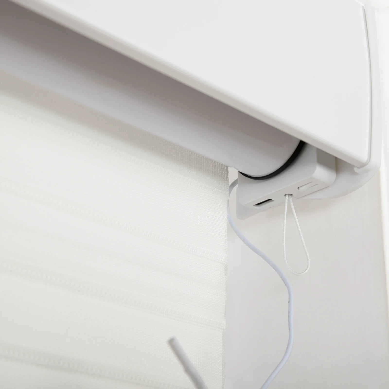 Close-up of a white motorized window Blind mechanism with a sheer fabric Blind featuring subtle horizontal textured bands, showing a white power cable connected to the housing and a small white pull cord loop