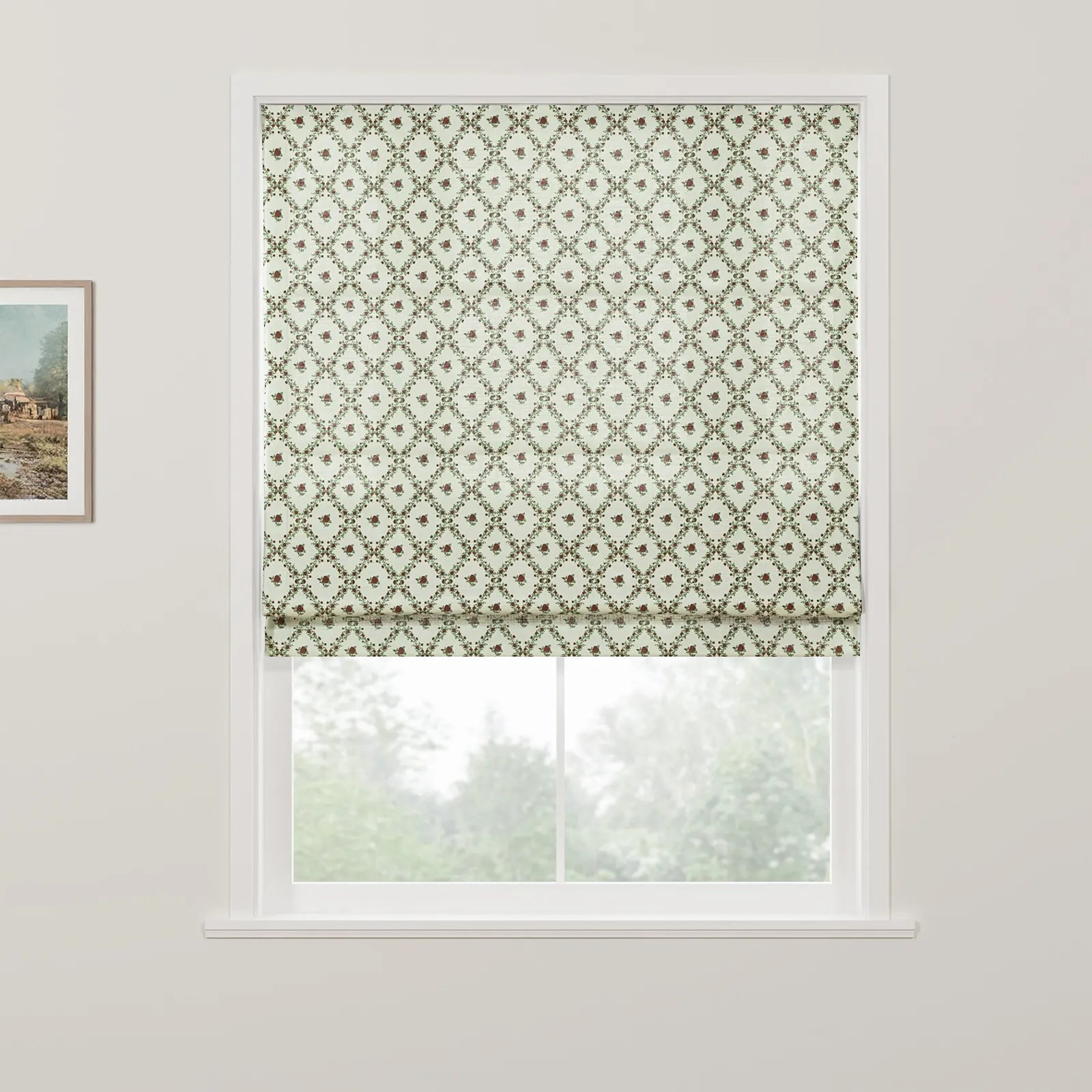 Photograph of an interior window featuring a light green Roman blind with a lattice pattern and small red floral motifs, a framed landscape painting hangs on the left wall