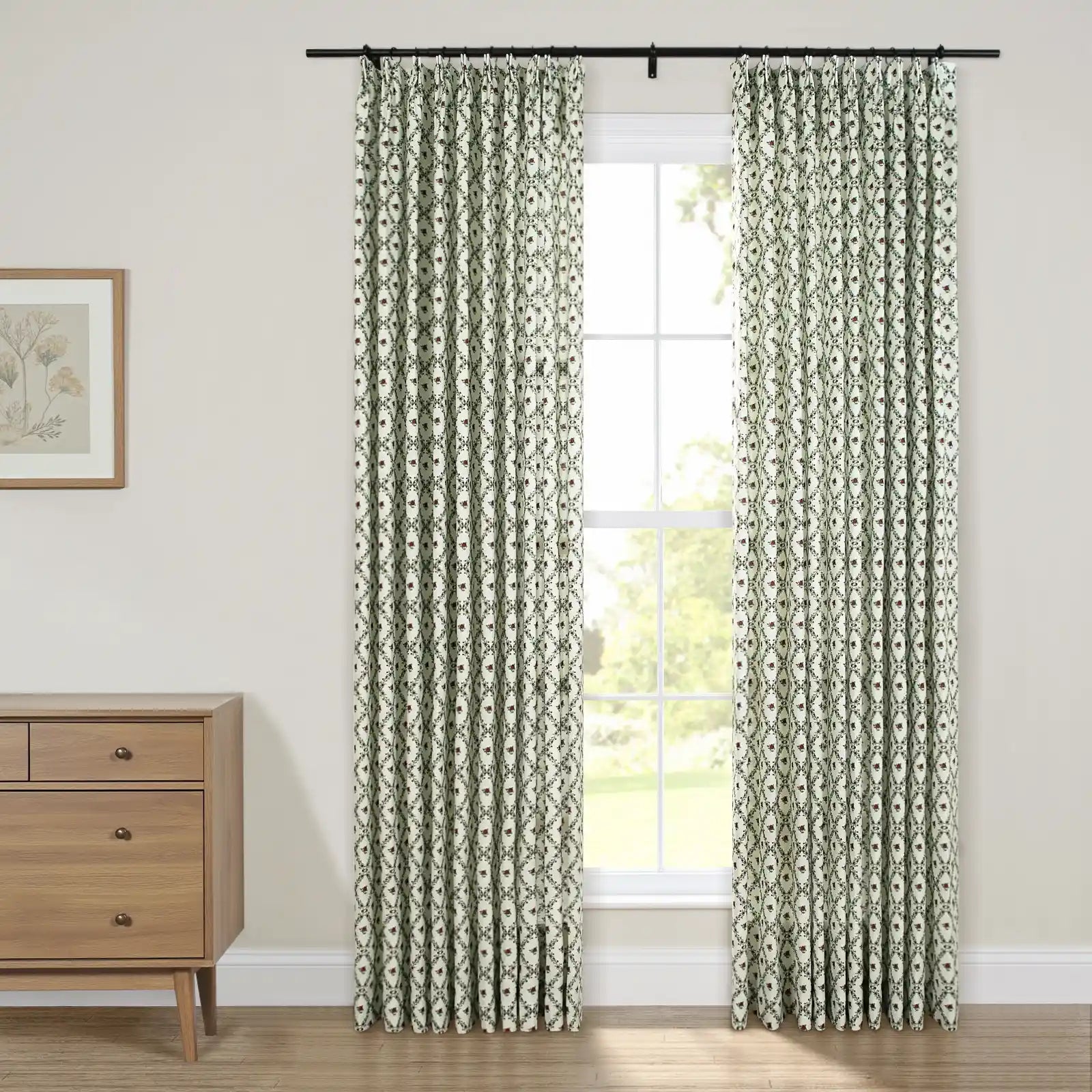 Green and white patterned curtains with a repeating oval floral print hang on a black rod over a bright window next to a light wood dresser and botanical art
