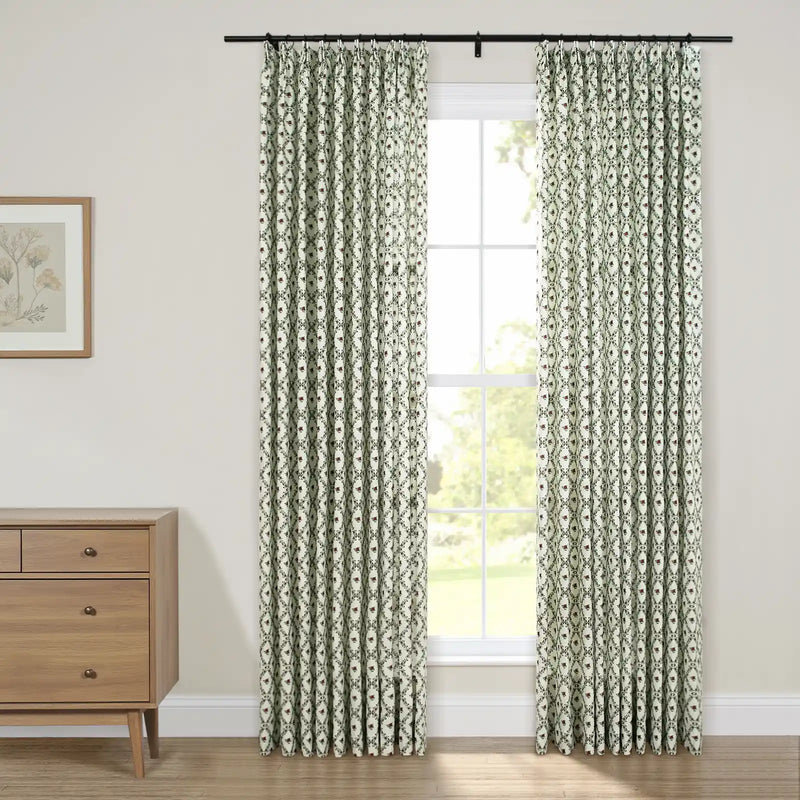 Green and white patterned curtains with a repeating oval floral print hang on a black rod over a bright window next to a light wood dresser and botanical art