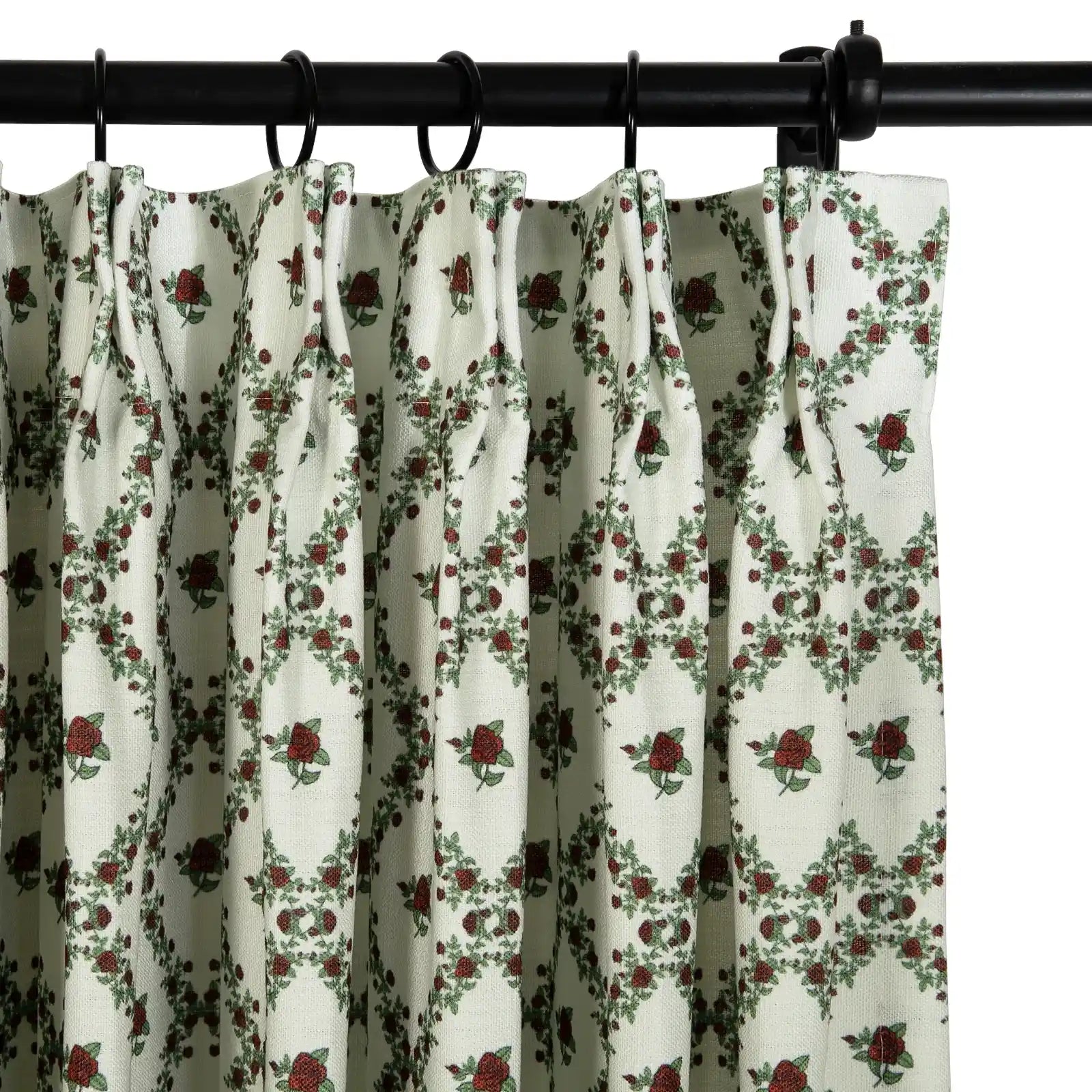 Photograph of a pleated cream curtain featuring a repeating pattern of deep red roses and green leaves hanging from a black rod with rings