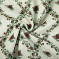 Fabric pattern of red roses and green leafy vines arranged in diagonals on a creamy white woven background with soft fabric folds