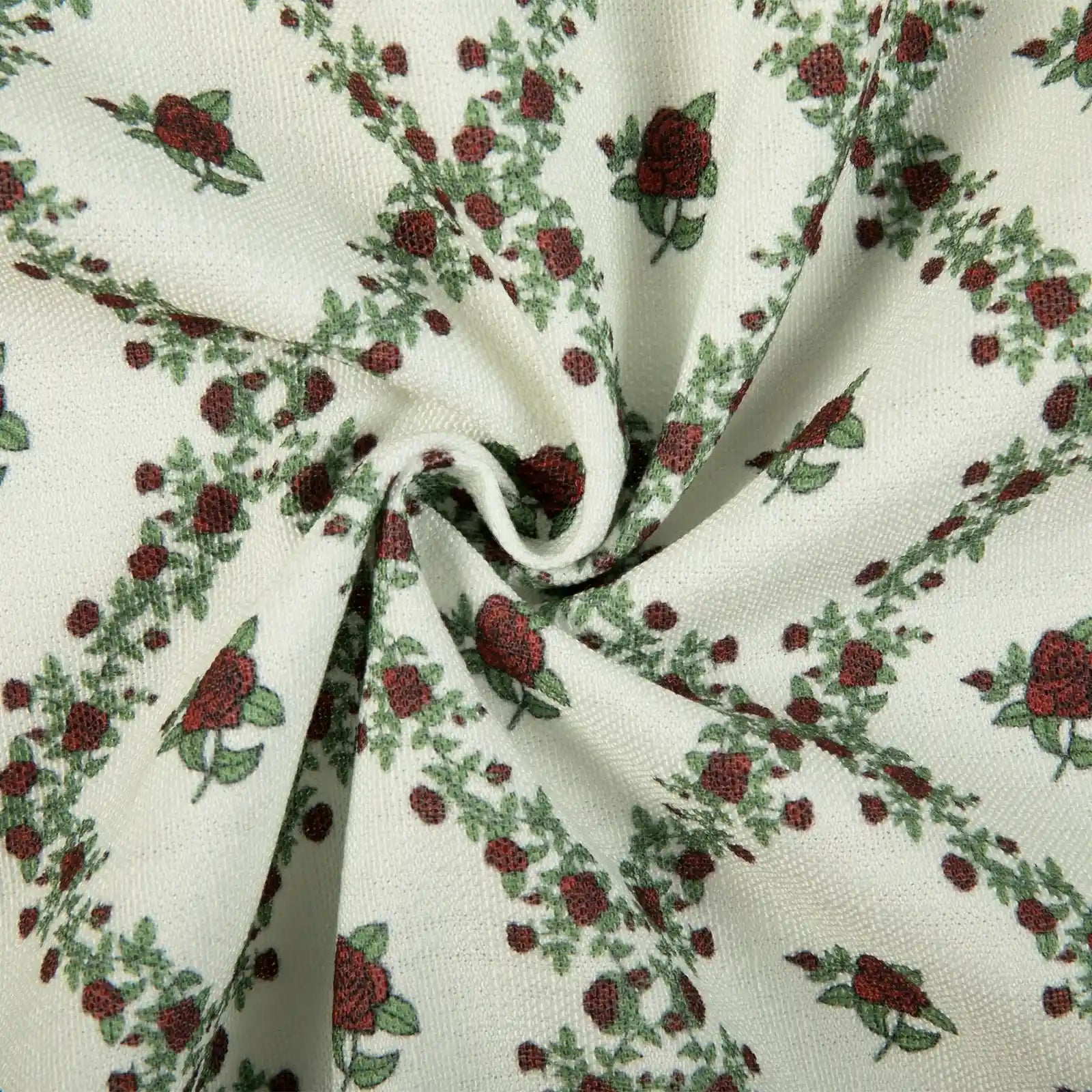 Fabric pattern of red roses and green leafy vines arranged in diagonals on a creamy white woven background with soft fabric folds