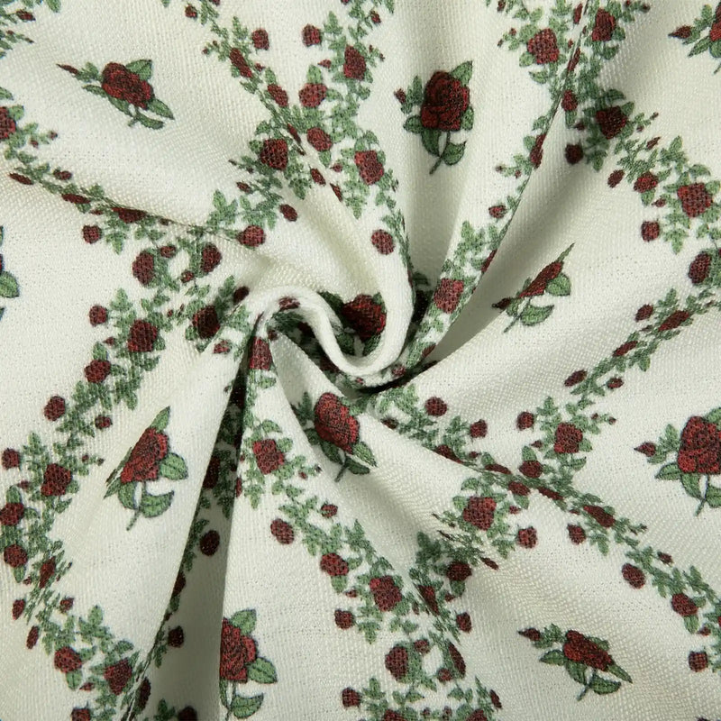 Fabric pattern of red roses and green leafy vines arranged in diagonals on a creamy white woven background with soft fabric folds
