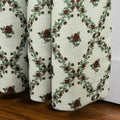 Textile print of a pleated off-white textured fabric curtain featuring a repeating pattern of deep red roses and green leafy vines forming diamond shapes above a dark wooden floor