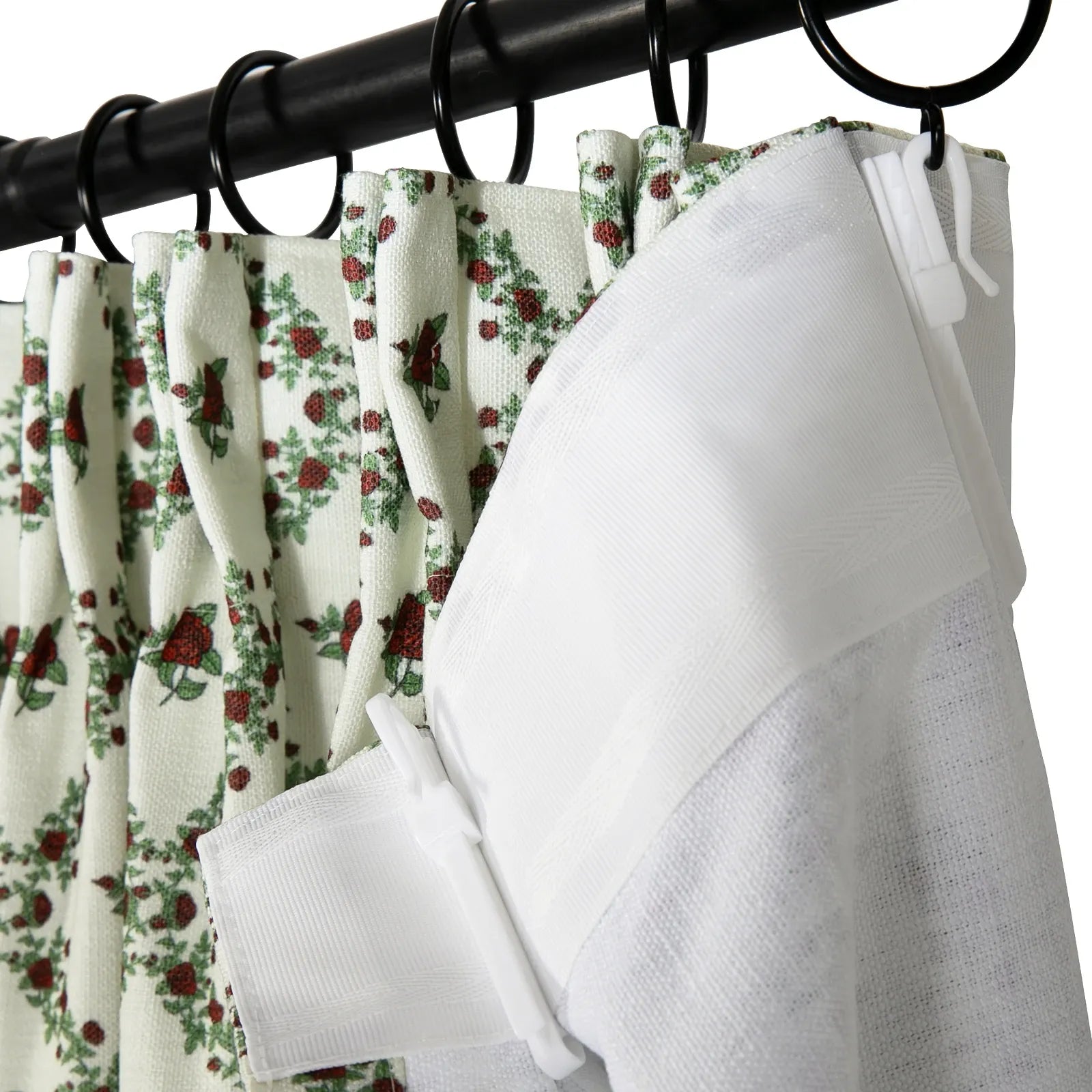 Close-up of pleated white curtains featuring a vibrant red rose and green leaf pattern, alongside a textured white liner, all suspended from a black curtain rod by black rings and white plastic hooks