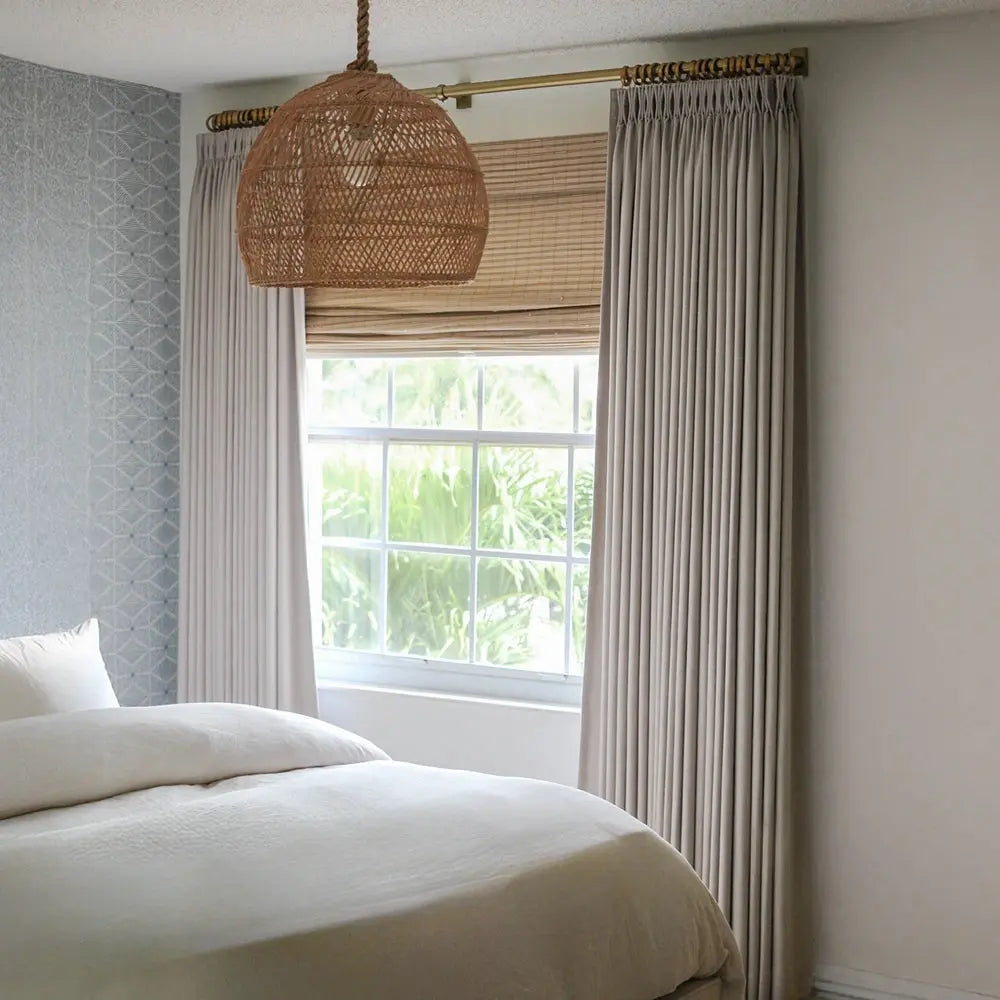 Photograph of a calming bedroom interior with a woven wicker pendant light, a window framing lush green foliage, and a light blue geometric patterned accent wall