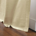 Cream curtain with a subtle sheen draped on a dark brown wooden floor next to a white baseboard with visible stitched details