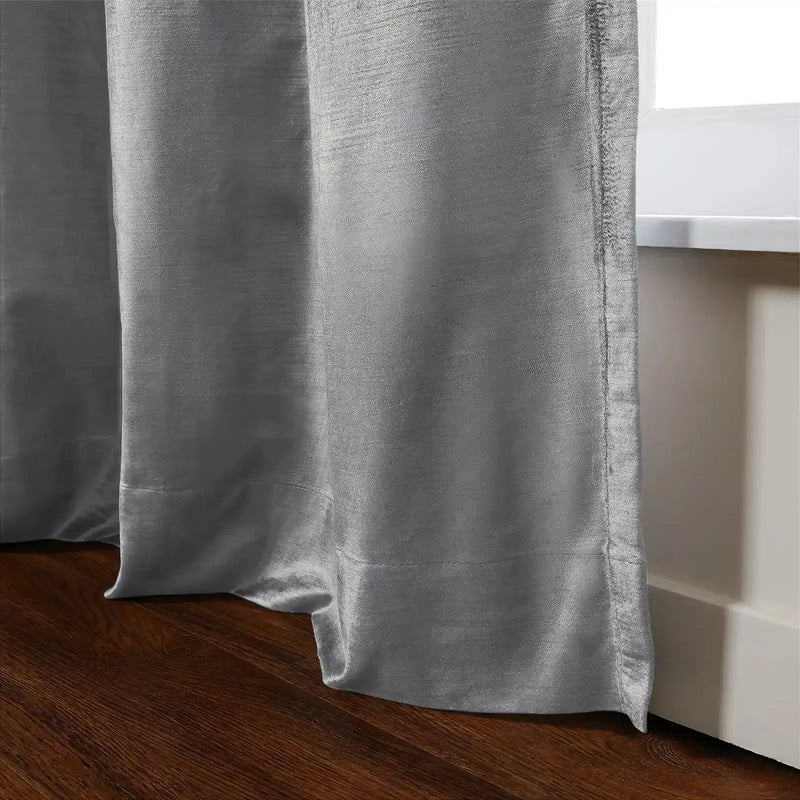 View of a luxurious silver-grey curtain with a subtle shimmer falling in soft folds onto a polished dark wooden floor next to a bright white window frame
