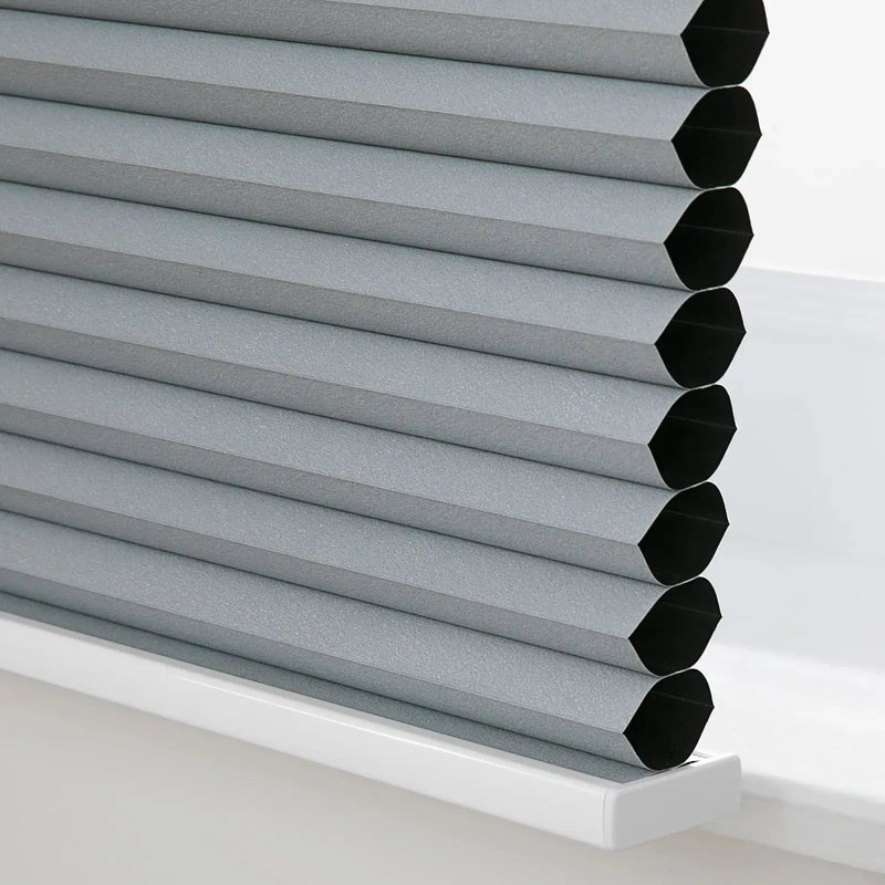 Photograph of textured grey cellular honeycomb window Blinds revealing black interior cells resting on a white windowsill