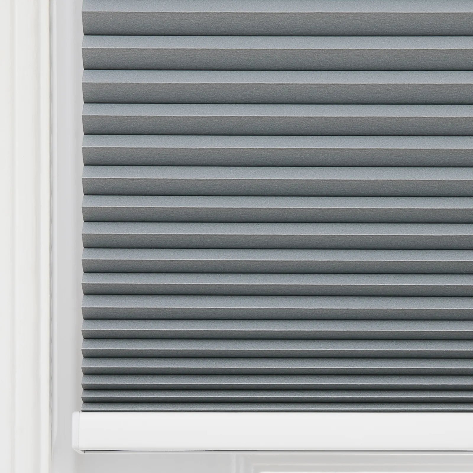 Grey cellular window Blind featuring neat horizontal pleats, textured fabric, a white window frame edge, and a white bottom rail