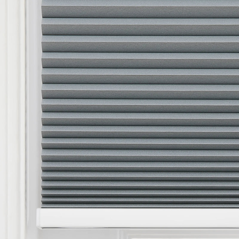 Grey cellular window Blind featuring neat horizontal pleats, textured fabric, a white window frame edge, and a white bottom rail