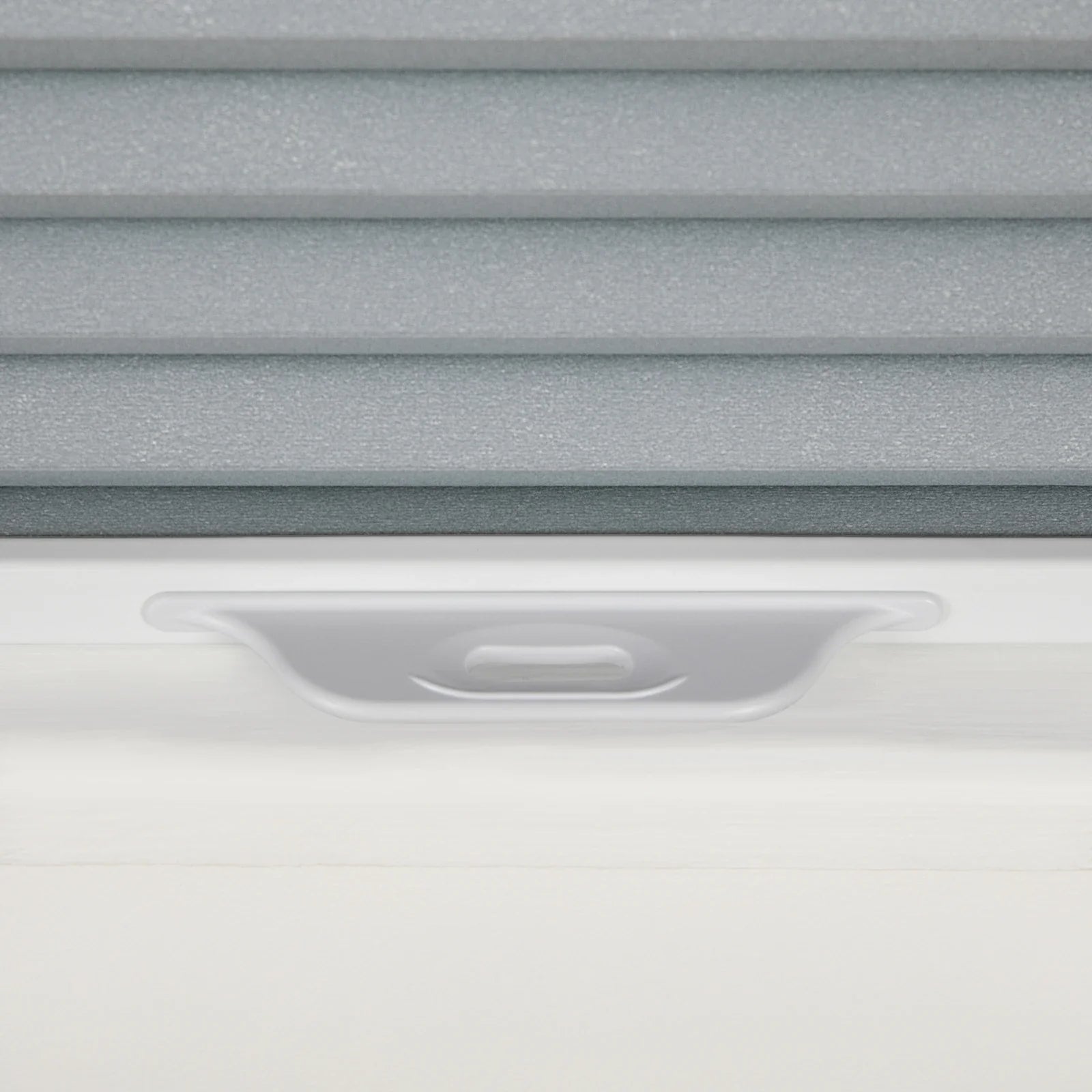 Close-up of gray textured cellular pleated window Blinds with a white frame and an integrated gray adjustment handle