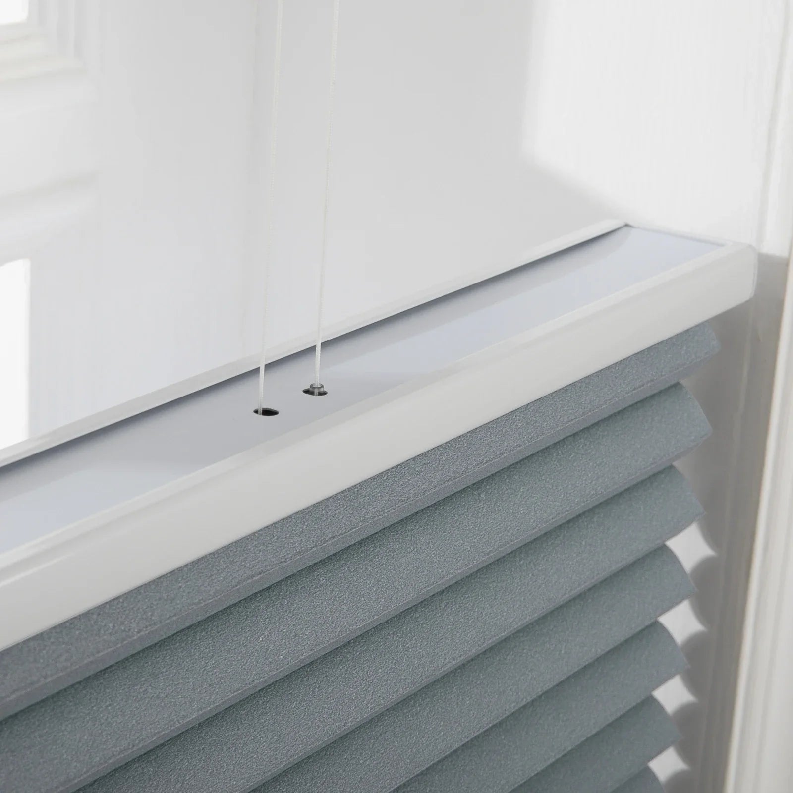 Photograph of modern cellular window Blinds in an interior setting featuring textured grayish-blue fabric a sleek white top rail and thin control cords