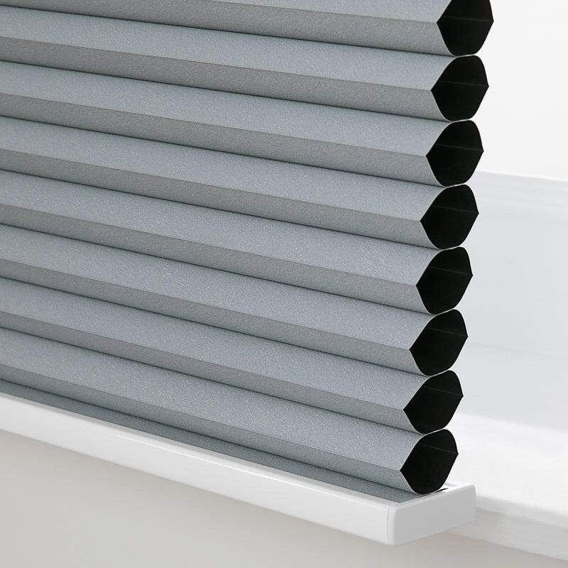 Gray cellular Blinds with a textured finish revealing black honeycomb interior cells resting on a clean white window sill