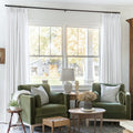 Snow White Liz Linen Pleated Curtains framing a green sofa beneath a wide sunlit window