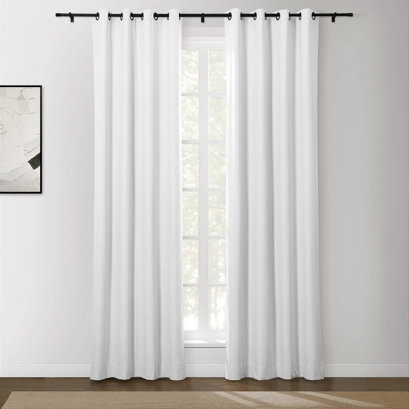 White grommet top curtains on a sleek black rod in a modern room with abstract monochrome wall art and a sunlit view of outdoor greenery