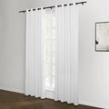 Photograph of a bright room featuring white grommet-top curtains on a black rod covering a window with a dark wood floor and a framed abstract black and white artwork on the right wall