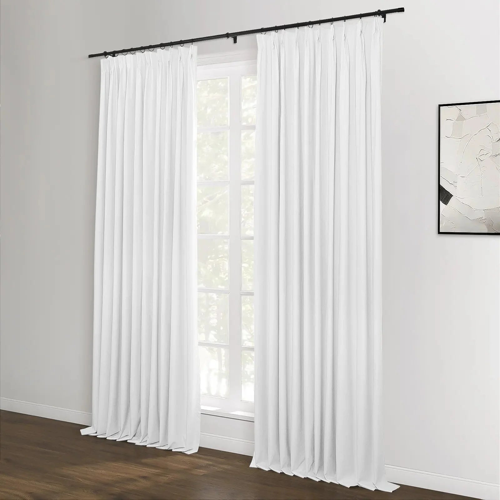 White pinch-pleat curtains on a black rod frame a large window with green foliage visible outside, complementing a modern room with dark wood flooring and abstract monochrome artwork