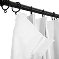 White pleated curtains with visible texture attached by white plastic hooks to black metal rings on a black curtain rod