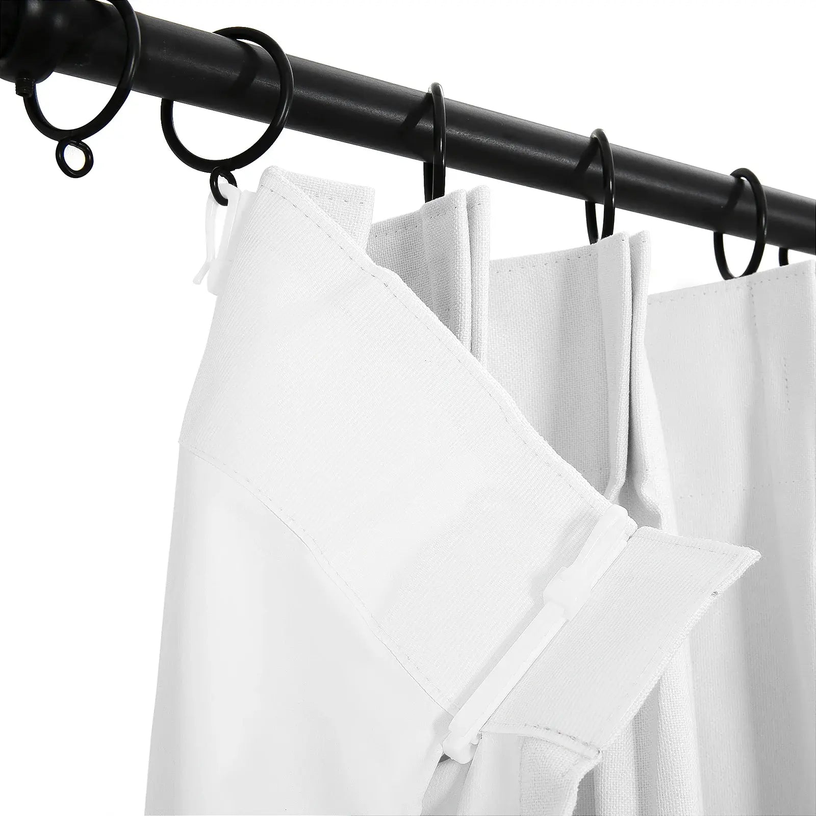White pleated curtains with visible texture attached by white plastic hooks to black metal rings on a black curtain rod