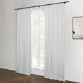 A room featuring white blackout curtains with a black rod and rings over a window, complemented by dark hardwood floors and an abstract black and white artwork