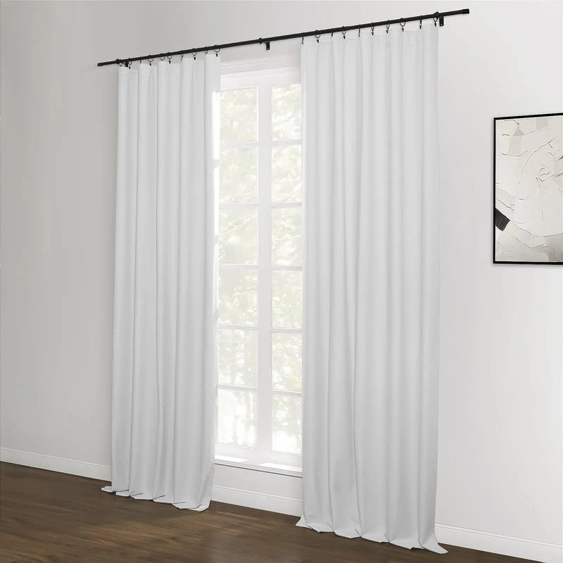 A room featuring white blackout curtains with a black rod and rings over a window, complemented by dark hardwood floors and an abstract black and white artwork
