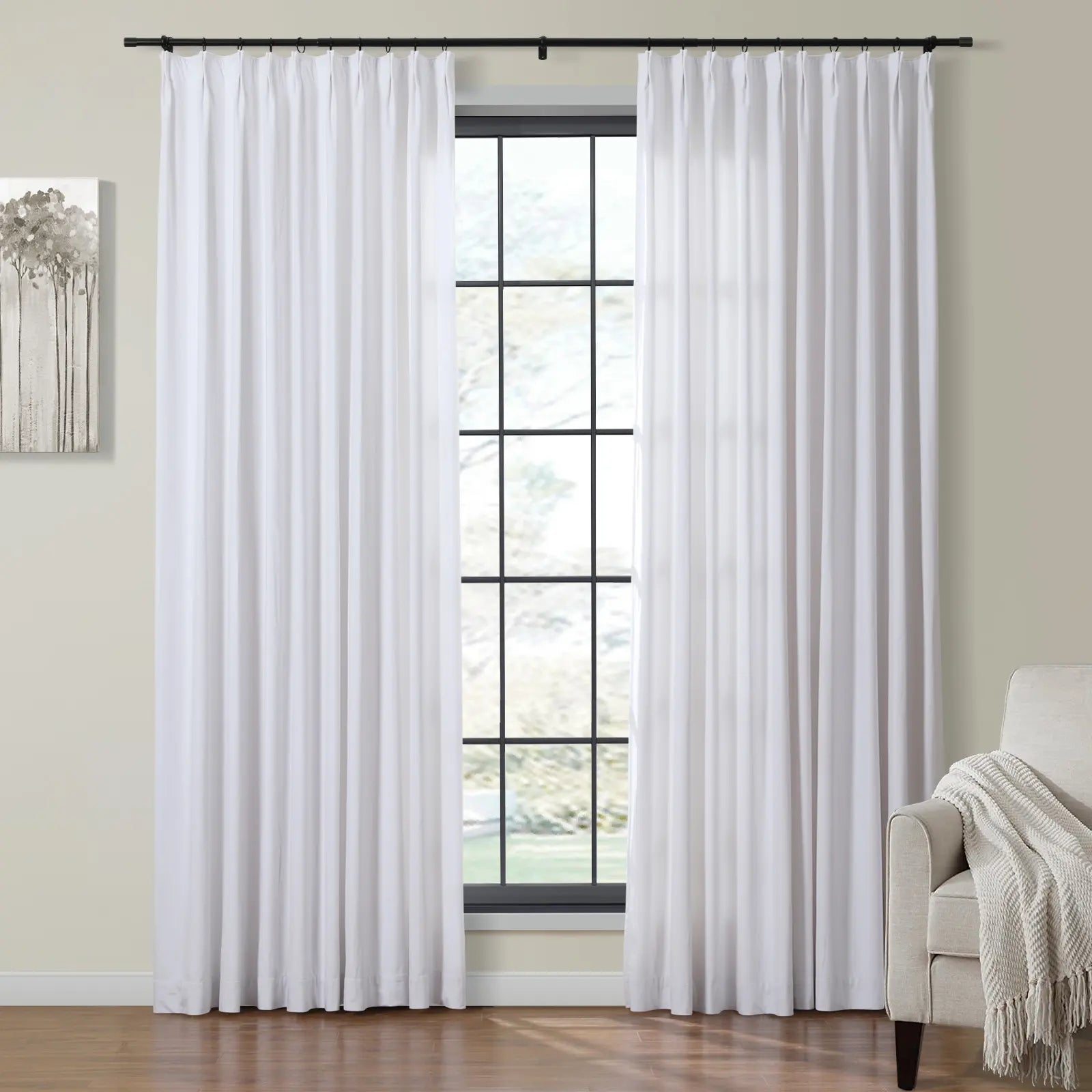 White pleated curtains hang on a black rod framing a large grid-paned window in a contemporary room featuring abstract tree artwork and a beige armchair with a cream throw
