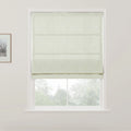 Pale green Roman blind with a subtle scroll pattern in a white window frame overlooking blurred green trees