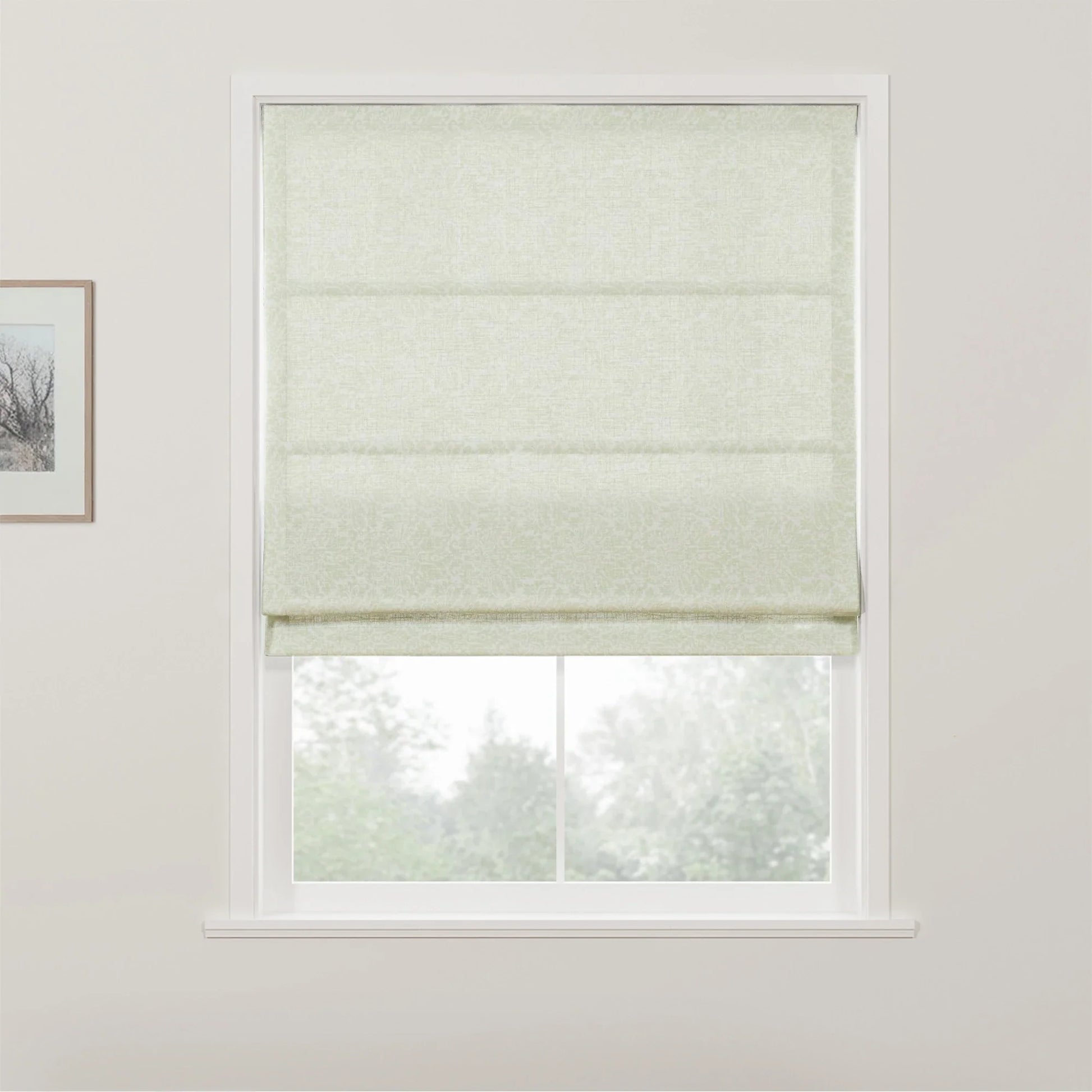 Pale green Roman blind with a subtle scroll pattern in a white window frame overlooking blurred green trees