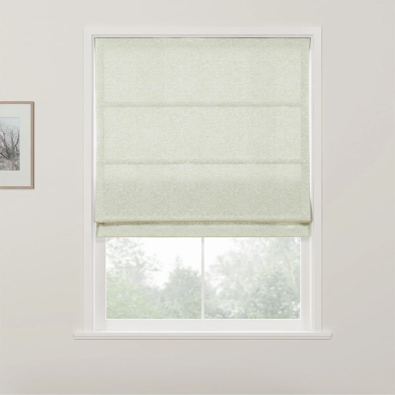 Pale green Roman blind with a subtle scroll pattern in a white window frame overlooking blurred green trees