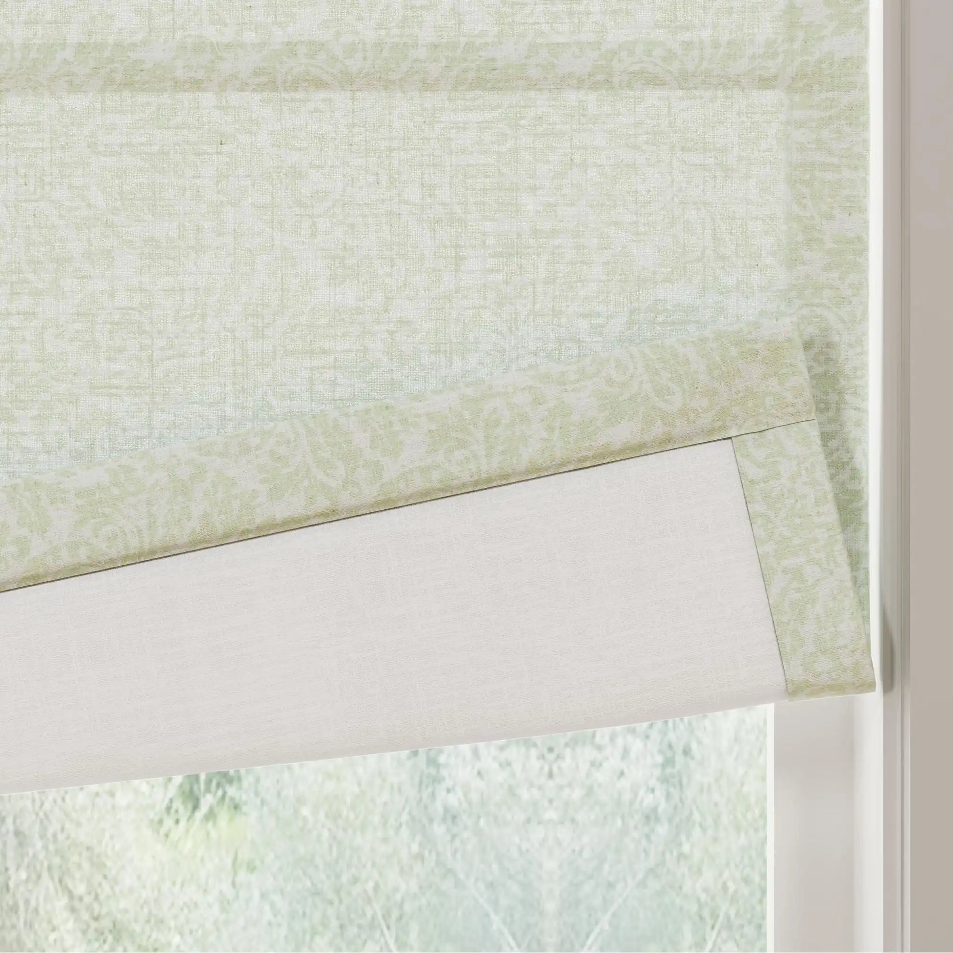 A light green patterned Roman shade featuring a subtle botanical damask print with a solid white lining partially lowered against a window