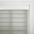 A light grey zebra sheer window Blind with alternating opaque and sheer horizontal stripes installed within white decorative window trim showing a subtle yellow tip on the control cord